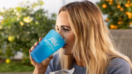 A young woman drinking a glass of water, the cup has the words Mesa Water upon it.